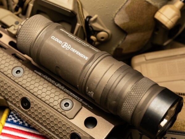 Czarna latarka taktyczna zamontowana na szynie RIS karabinu z jasnym strumieniem światła