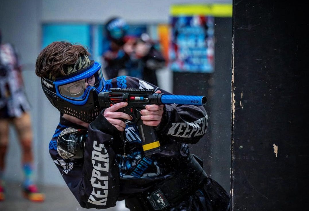 gracz w kolorowym kombinezonie paintball biegnący za barykadą