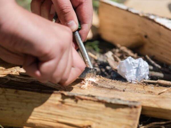mężczyzna w lesie klęczy przy stosie suchego drewna i rozdmuchuje płomień